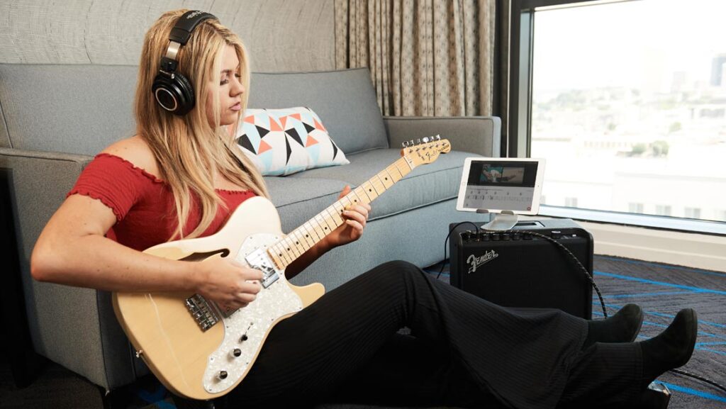 Mujer tocando su guitarra con su tablet y auriculares, usando apps para hacer una canción.