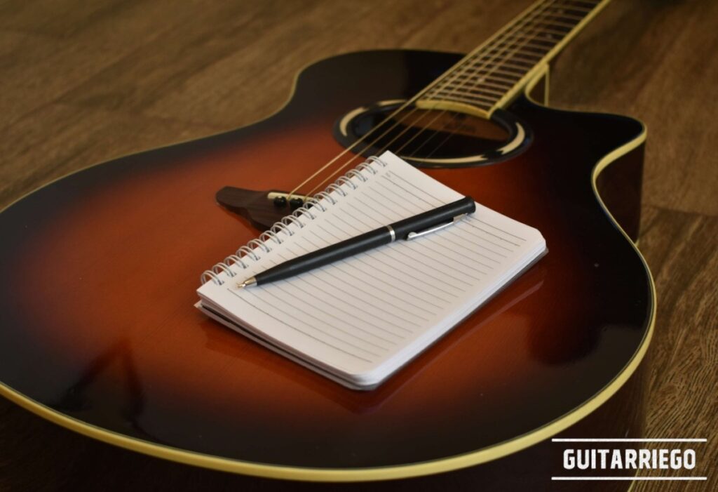 Gitarre mit Notizblock und Stift oben, die den Prozess des Schreibens deiner Songtexte widerspiegeln.